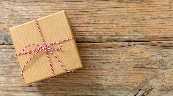 Christmas gift box on wooden background. Red white striped string tied on brown  kraft present. Stock Photo by rawf8