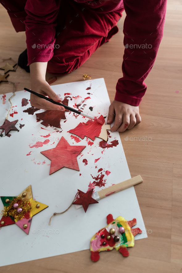 Young child painting Christmas decorations kneeling down on the floor