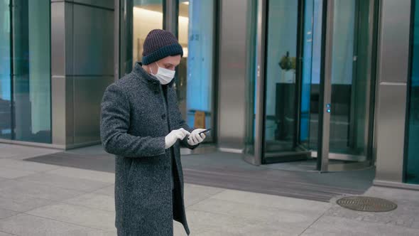2019-Ncov: Business Man in Surgical Mask Uses App on Smartphone Walking Outdside