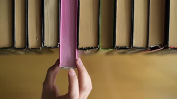 A girl takes a book with pink pages from a shelf and puts it back in a row alt