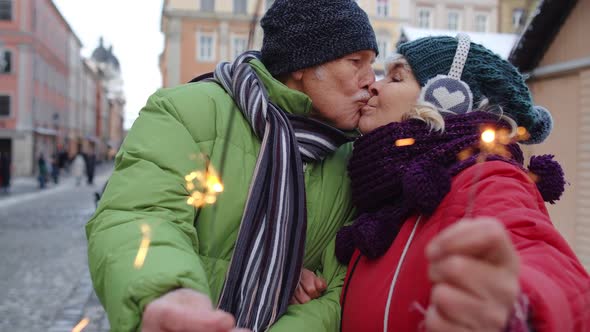 Senior Couple Holding Sparklers Bengal Lights Enjoying Christmas Eve Making Kiss in Winter City alt