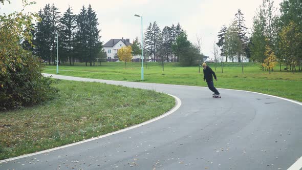 Adult Gray-haired Man Rides a Skateboard on a Path in a Forest Park, Autumn Time of the Year, Man alt