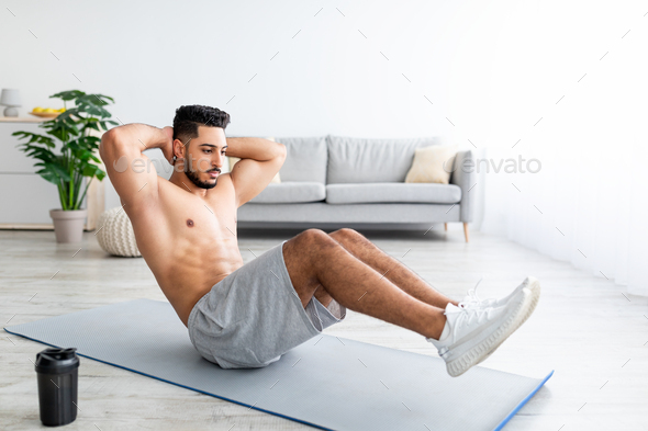 Full length of fit Arab man strengthening core muscles, doing abs ...