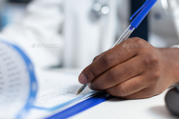 Closeup of african american doctor hand analyzing ill symptoms writing medical treatment