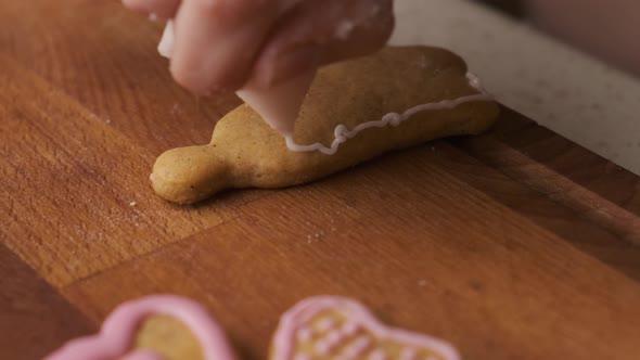 Woman Decorates a Gingerbread in the Shape of Bell on the Wooden Desk with Icing alt
