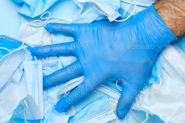 Mans hand in rubber blue glove on a background of used protective face masks. Medical trash after