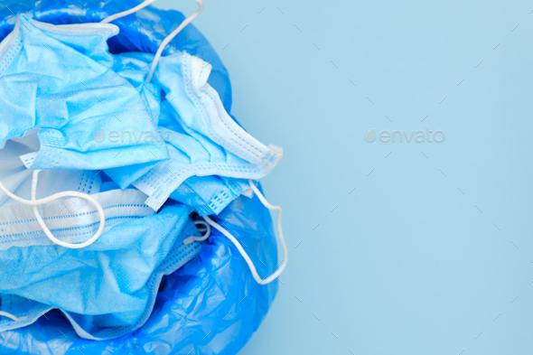 Used disposable surgical mask in a trash bucket on a blue background with copy space. Over of