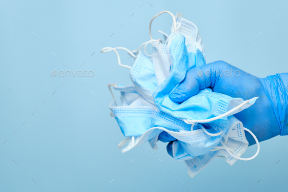 Man hand in rubber blue gloves holding used disposable protective masks on a blue background with