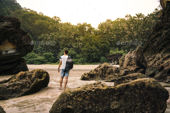 Man with backpack between big stones near green trees - Stock Photo - Images