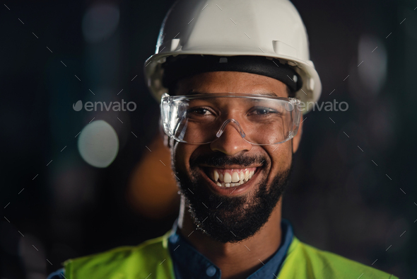 Happy young industrial man with protective wear indoors in metal workshop, looking at camera. - Stock Photo - Images
