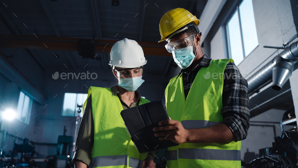 Inspectors with face masks doing a general check up at metal workshop, coronavirus concept.