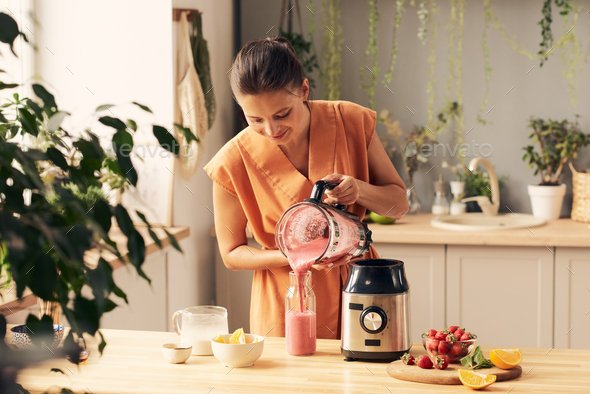 Woman in orange dress pouring fresh milk into electric blender Stock Photo  by Pressmaster