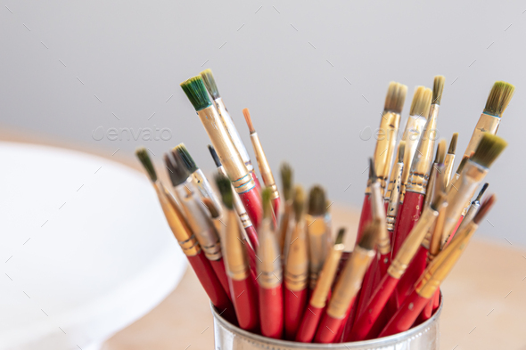 Close-up of red paint brushes in a metal jar. Stock Photo by puhimec