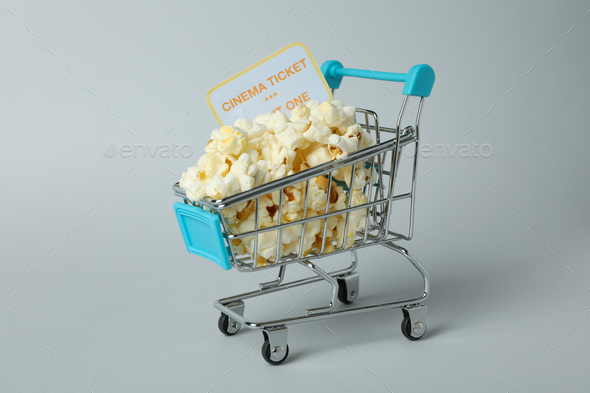 Shop trolley with popcorn and ticket on light gray background