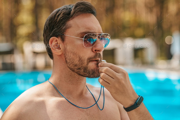 Male lifeguard in sunglasses near the public swimming pool Stock