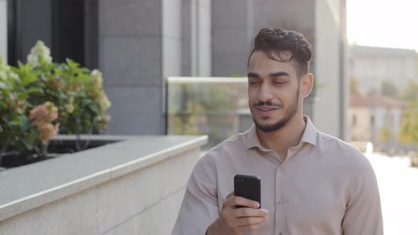 Hispanic Business Man Smiling Walking City Street Looking at Mobile Phone Online Map Application App alt