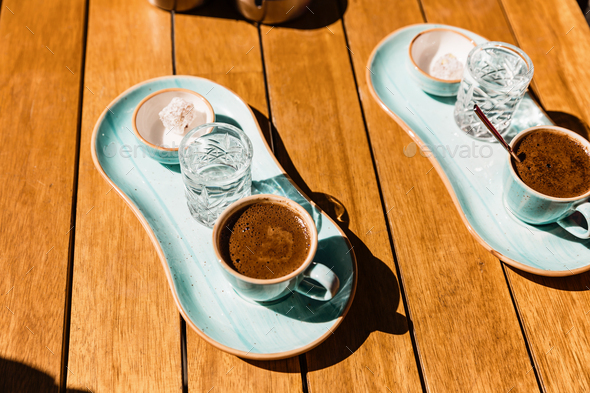 a cup of hot black turkish coffee in blue cup served with glass of water and sugar