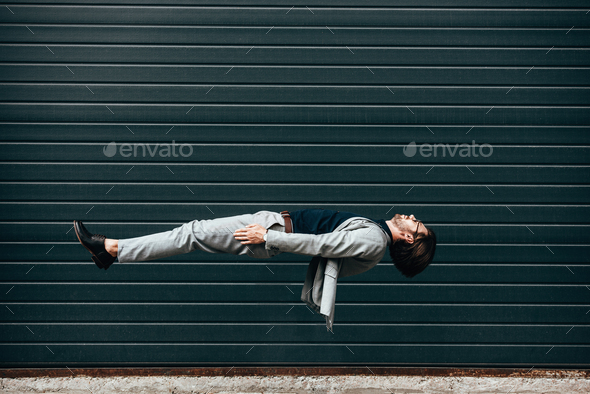 side view of young businessman lying on back in air in front of roller gate