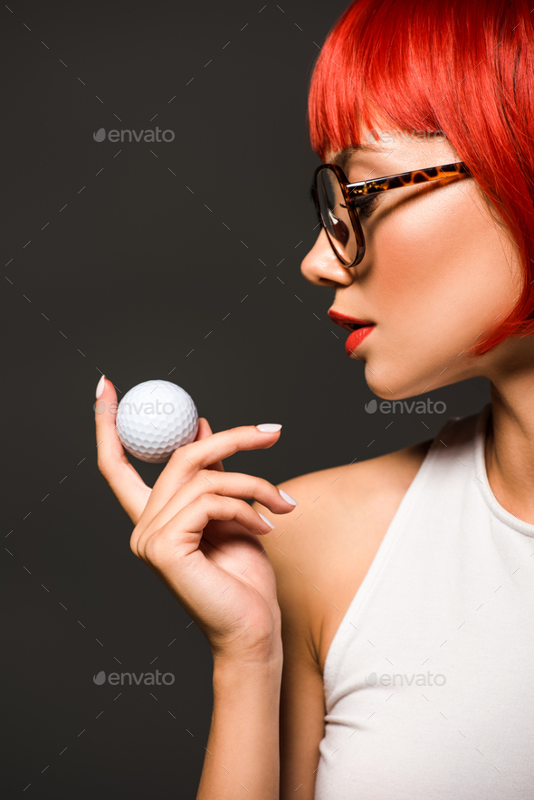 close-up portrait of beautiful young woman with red bob cut and stylish eyeglasses holding golf ball