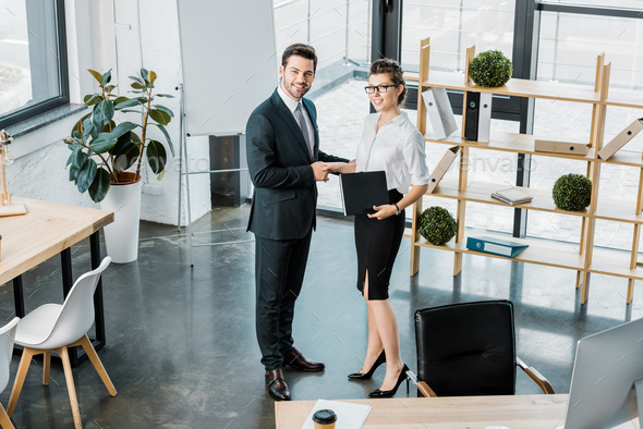 high angle view of smiling business colleagues shaking hands in office - Stock Photo - Images