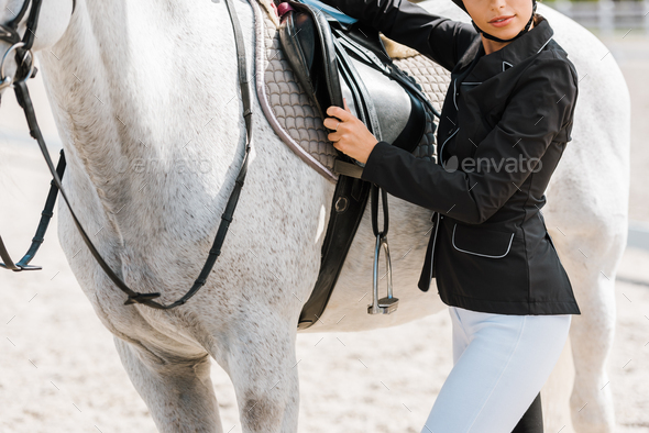 cropped image of female equestrian fixing horse saddle at horse club