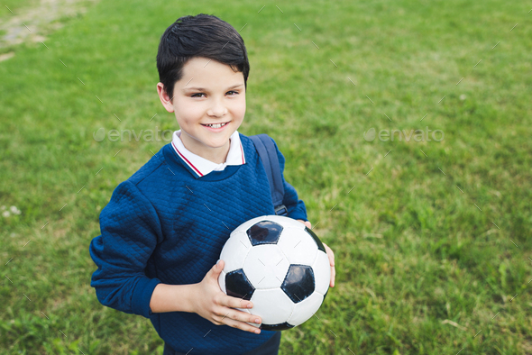 happy kid holding soccer ball and looking at camera on grass field ...