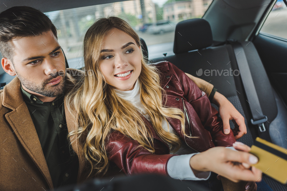 stylish young couple sitting together in taxi, girl holding credit card