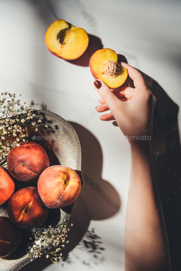 cropped shot of woman with piece of peach in hand and bowl full of ripe peaches and gypsophila