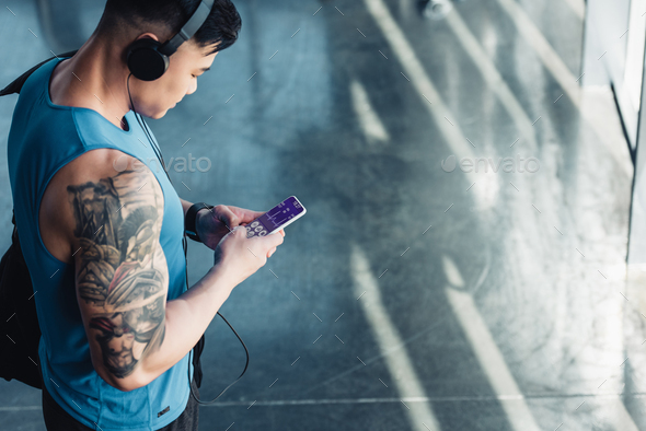 young sportsman using smartphone with health data appliance app and listening to music