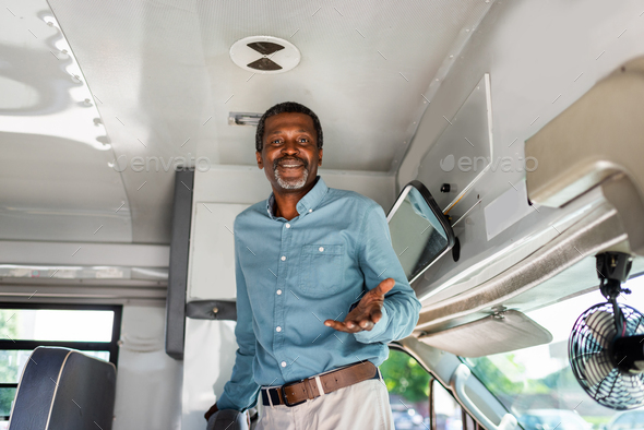 happy mature african american bus driver standing inside bus and looking at camera