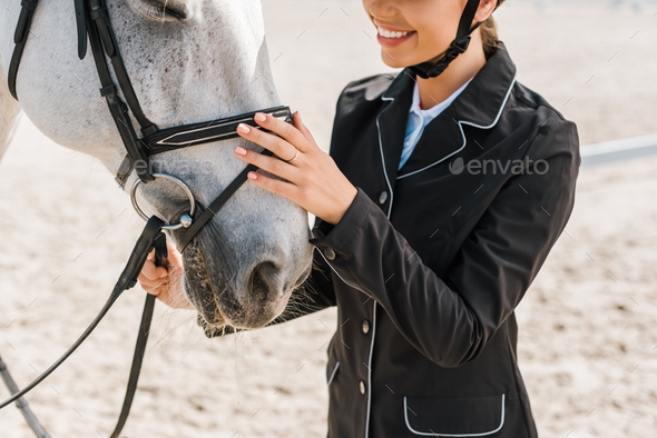 cropped image of smiling female equestrian palming horse at horse club