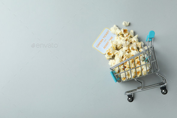 Shop trolley with popcorn and ticket on light gray background