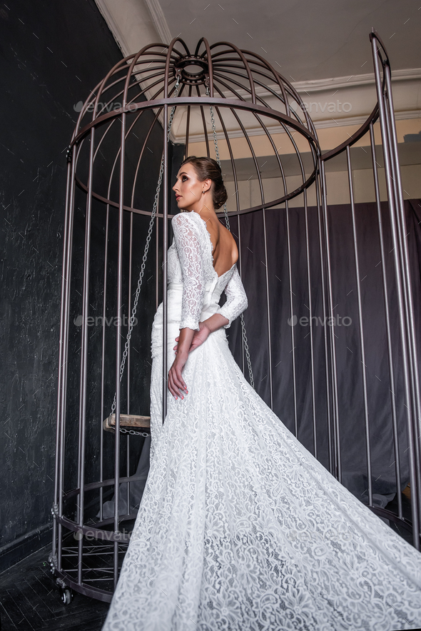Fashion bride in an iron cage, unhappily looking out from behind bars. Life out of will.