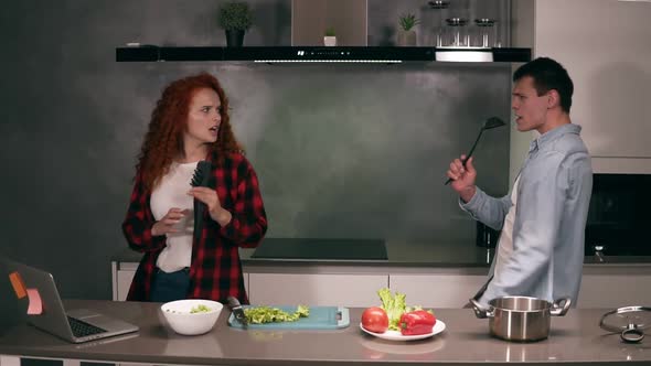 Happy Carefree Young Family Couple Husband and Wife Singing in Soup Ladle and Pasta Tongs Microphone alt