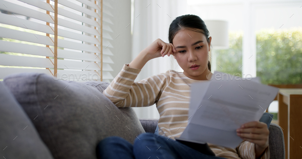 Upset tired young asia sad lady people sit sofa couch at home think hard worry in tax
