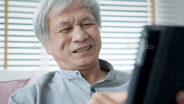 Candid old asian retired guy use tablet computer to transfer money online