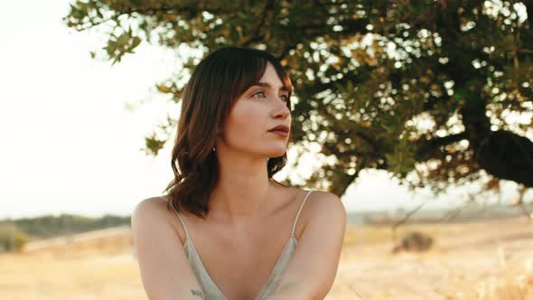 Beautiful Girl Sitting in the Shade of a Tree in the Countryside Relaxes alt