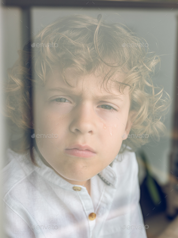 Sad little boy looking through glass - Stock Photo - Images