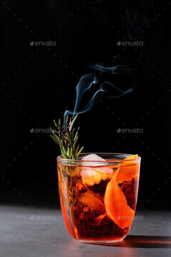 Negroni cocktail with smoking rosemary and orange garnish on black