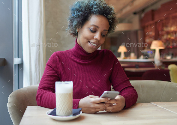 African american woman surfing internet or using app with her phone in cozy cafe