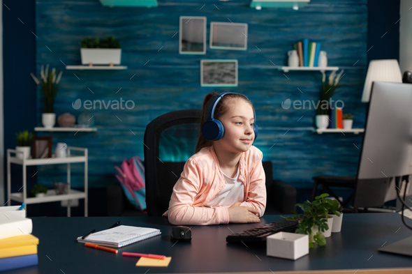 Little child wearing headphones having online math lesson on computer