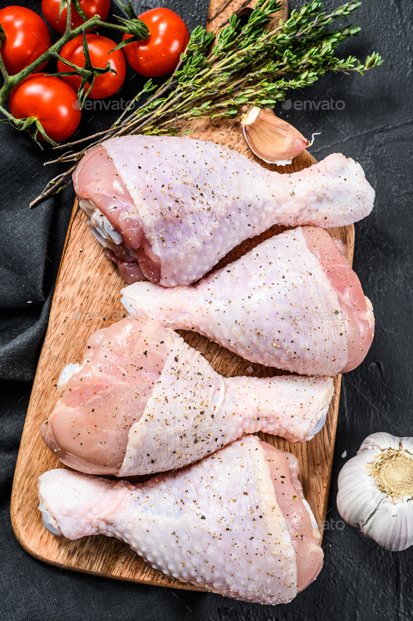 Raw chicken legs with spices and vegetables on a wooden cutting board. Black background. Top view - Stock Photo - Images