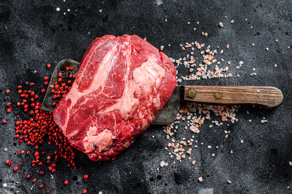 Raw Chuck eye roll steak on meat cleaver. Organic beef. Black background. Top view