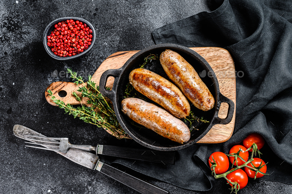 Tasty homemade sausages in a skillet. Pork, beef and chicken meat. Black background. Top view