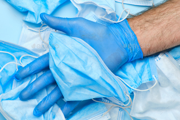 Mans hand in rubber blue glove holding used disposable surgical mask on a background of other face