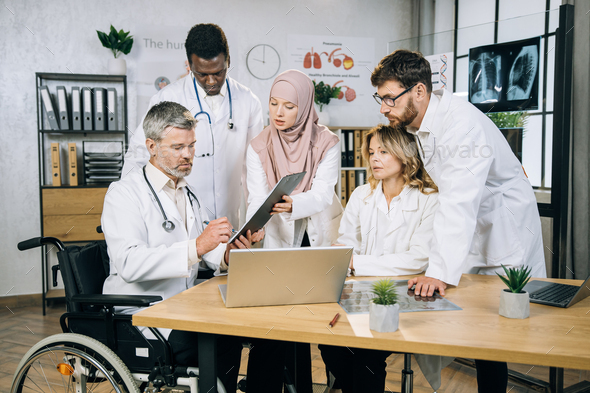 Mature head doctor in wheelchair with colleagues at office - Stock Photo - Images