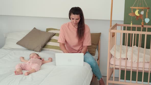 Busy Mom Works Using Laptop While Baby Sleeps Next to Her alt