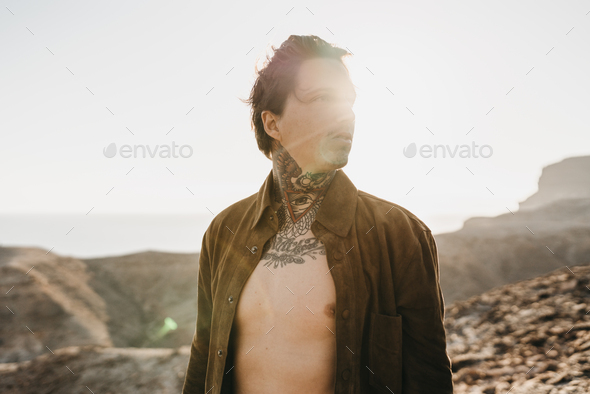 Handsome tattooed man standing on rocky shore