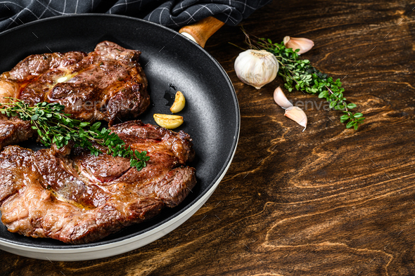 Grilled marble meat steaks Chuck eye roll in a pan. Dark wooden background. Top view. Copy space