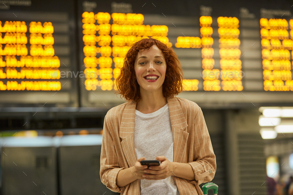 Red haired young woman using smartphone at station - Stock Photo - Images
